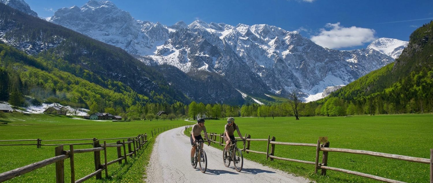Two gravel cyclists riding side by side along a valley road in the Kamnik-Savinja Alps